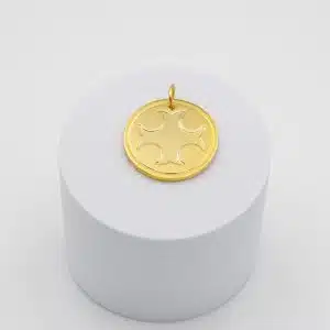 Médaillon croix templière doré posé sur un socle blanc, motif de croix en relief