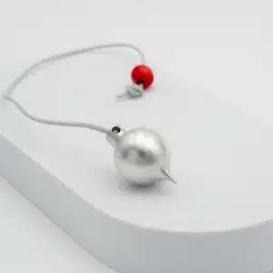 Pendule BT aluminium posé sur un présentoir blanc, corps argenté et perle rouge