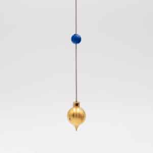 Pendule BT en laiton, corps doré effilé aux mesures du nombre d'or, suspendu à un cordon avec perle bleue